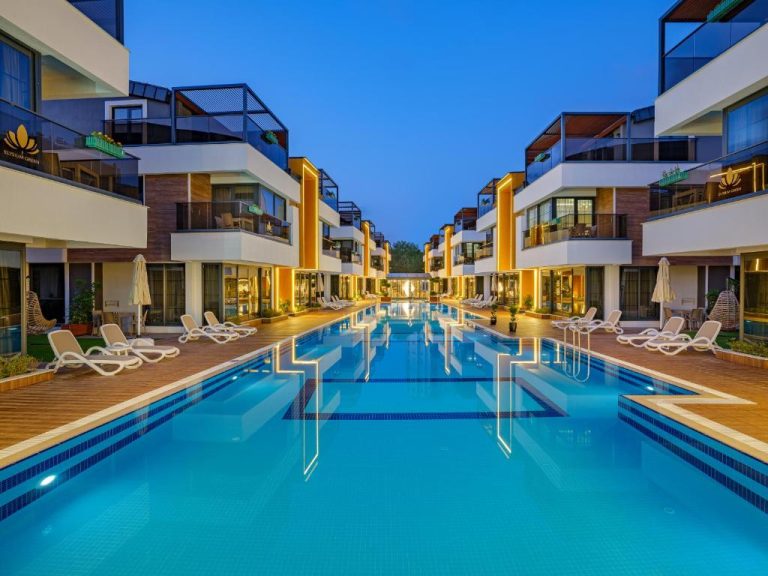 Piscina exterior iluminada de noche con tumbonas en Elysium Green Suites