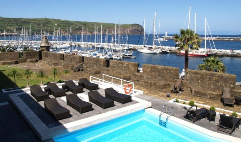 Piscina exterior con tumbonas y vistas al puerto deportivo de la Pousada Forte Horta en Azores