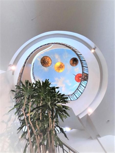 Atrio con escalera circular blanca y claraboya del I Pavilion Hotel Phuket con palmeras decorativas