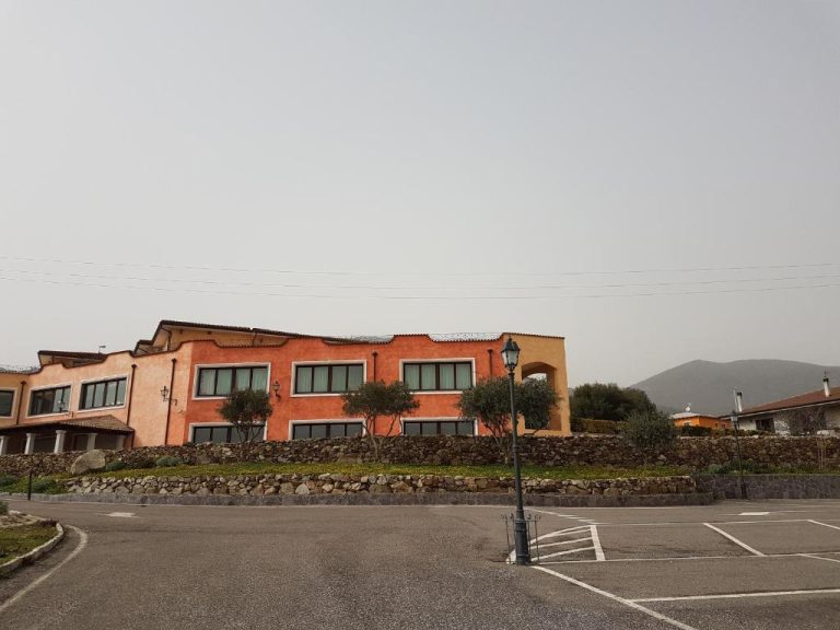 Fachada exterior del Hotel Le Tre Rose con aparcamiento, muro de piedra y jardín en Cerdeña