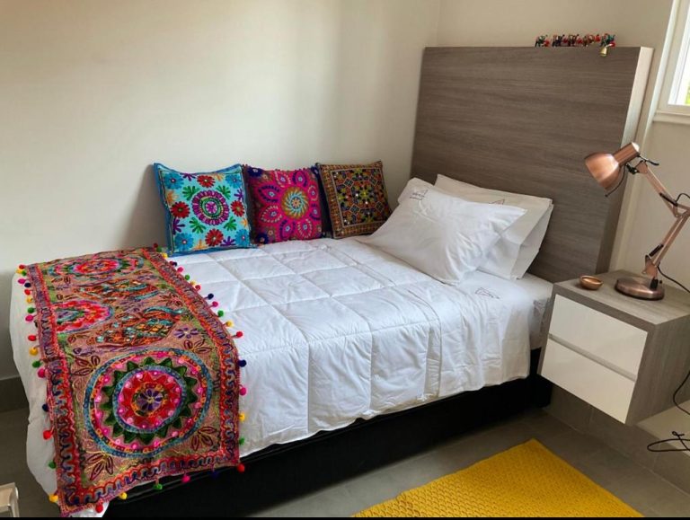 Habitación con cama doble, ropa de cama blanca y decoración colorida bohemia en Apartamento Encomenderos 200 Las Condes