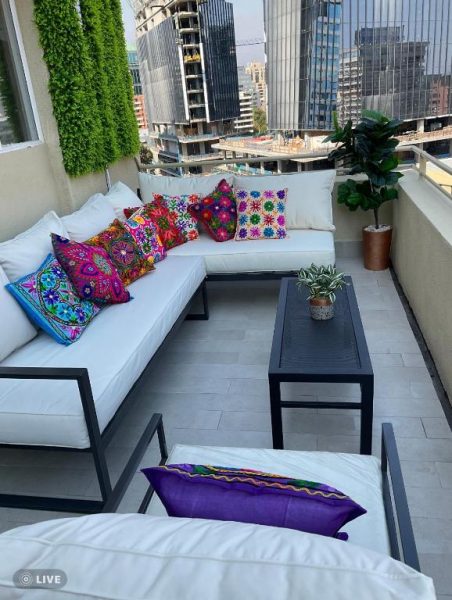 Terraza con sofás blancos y cojines coloridos con vista al Costanera Center en Apartamento Encomenderos El Golf Las Condes
