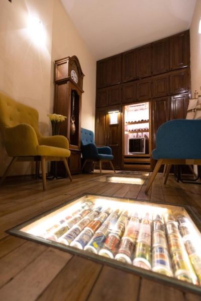 Salón de Casa El Edén con bodega de vinos bajo suelo de cristal iluminado y mobiliario vintage