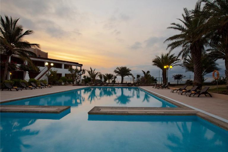 Piscina exterior del Pestana Trópico rodeada de palmeras y tumbonas al atardecer con vistas al mar