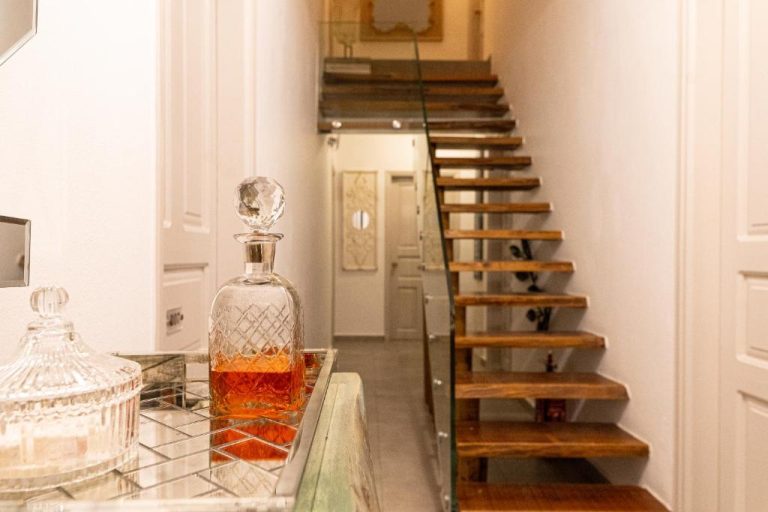 Elegante escalera de madera con barandilla de cristal y decantador de whisky en The Museum Project Oia