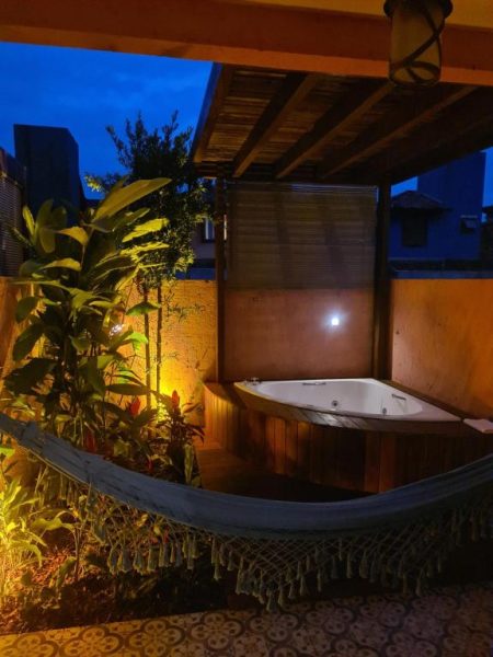 Jacuzzi exterior con hamaca y jardín iluminado de noche en Pousada Vila Rosada