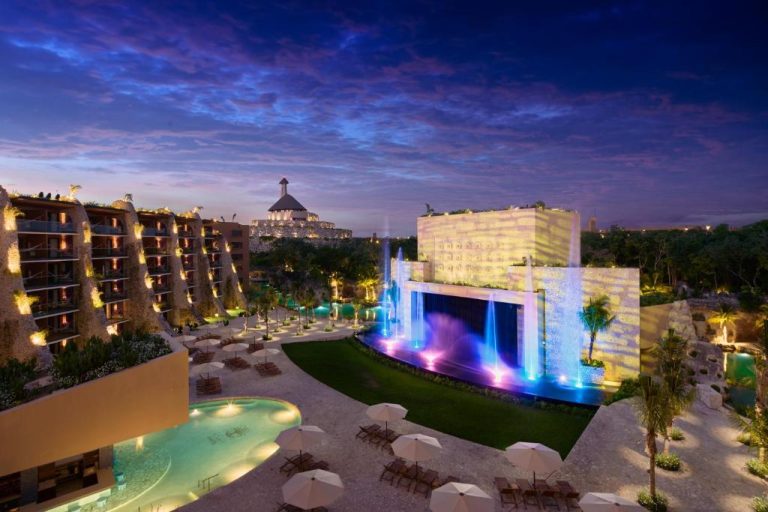 Vista nocturna de piscinas y fuentes iluminadas del Hotel Xcaret Arte Adults Only en México