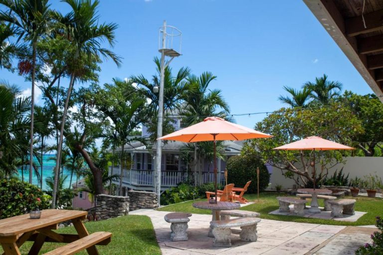 Terraza exterior con mesas de piedra y sombrillas naranjas en Orange Hill Beach Inn con vistas al mar