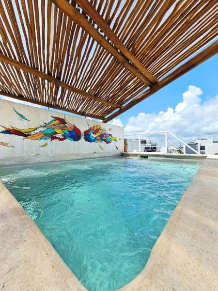 Piscina en azotea con mural artístico colorido y pérgola de madera en Hotel Playa Nah