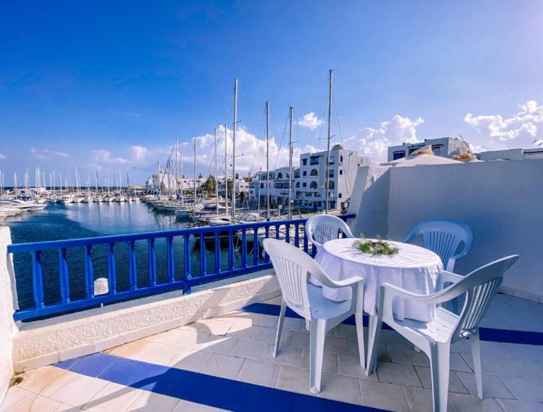 Terraza con mesa y sillas blancas con vistas al puerto deportivo en Marina Cap Monastir Appart'Hôtel