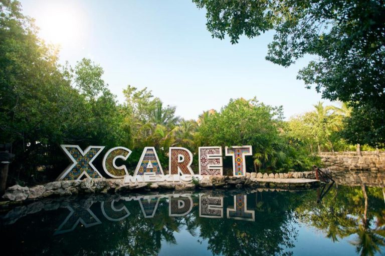 Cartel icónico de Xcaret México reflejado en laguna natural rodeada de vegetación tropical en Hotel Xcaret Arte
