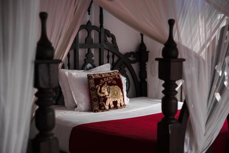 Habitación de lujo con cama de dosel de madera tallada y cojín bordado con elefante en Tembo House Hotel