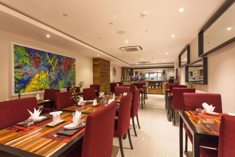Restaurante interior del The Somerset Hotel con mesas de madera, sillas rojas y arte moderno en la pared