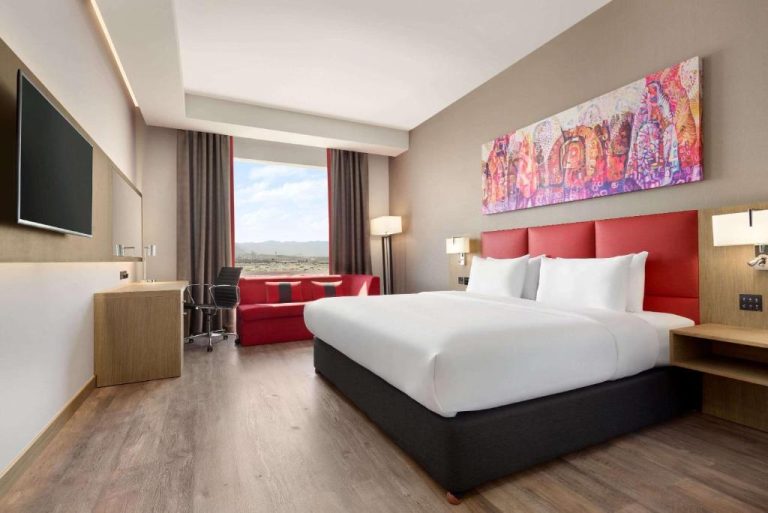 Habitación king size con cabecero rojo y vistas panorámicas en Ramada Encore by Wyndham Muscat Al-Ghubra