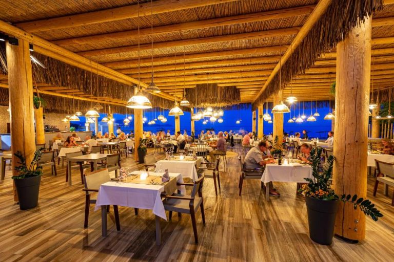 Restaurante de playa con techo de paja y vistas al mar nocturnas en Lindos Bay Hotel Rodas