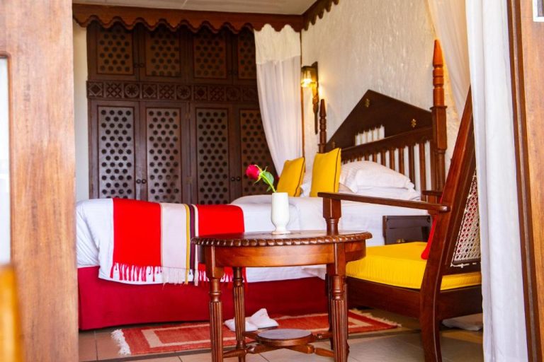 Habitación con cama con dosel de madera tallada y decoración tradicional swahili en Serena Beach Resort & Spa