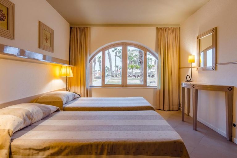 Habitación doble con camas individuales y ventana arqueada con vistas a las palmeras en Hotel Morabeza