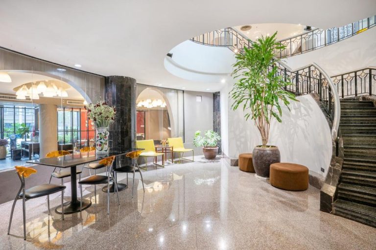 Elegante lobby con escalera curva de mármol y plantas tropicales en I Pavilion Hotel Phuket