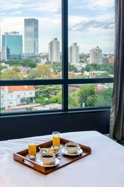 Bandeja de desayuno con café y jugo de naranja en habitación con vista panorámica al skyline del Hyatt Centric Montevideo
