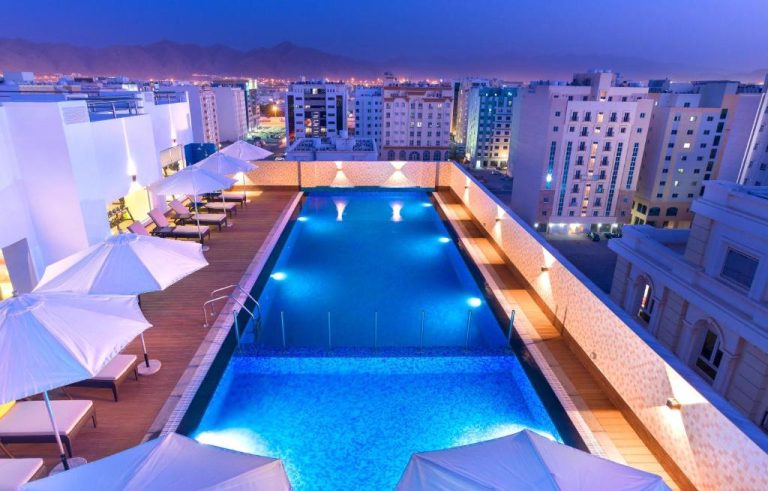 Piscina en la azotea del Centara Muscat Hotel Oman iluminada de noche con vistas a la ciudad