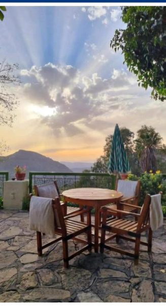 Terraza exterior con mesa de madera y vistas al atardecer sobre las montañas en Auberge des Cascades Imouzzer