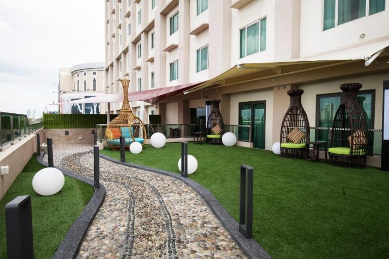 Terraza ajardinada con sillas colgantes de ratán y camino de piedra en el Ixora Hotel Penang