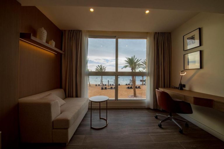 Habitación con sofá y escritorio con vistas a la playa y palmeras en Luxotel Aqaba Beach Resort & Spa