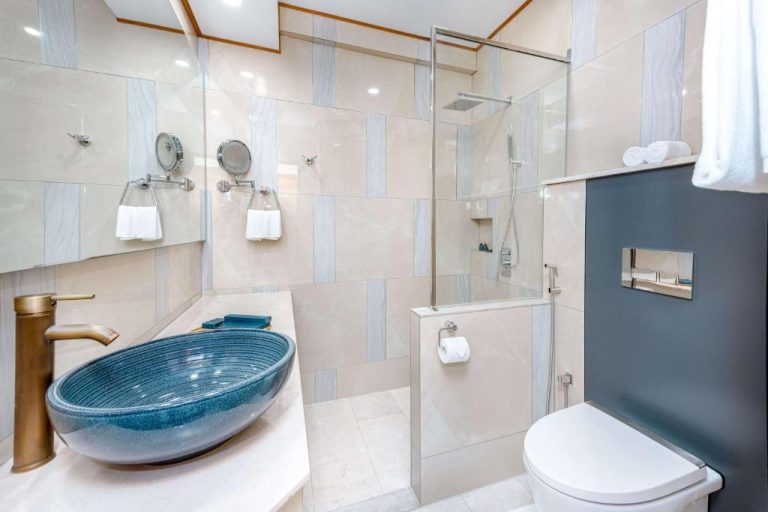 Baño moderno con lavabo azul artesanal y ducha de cristal en el hotel Marukab Plaza