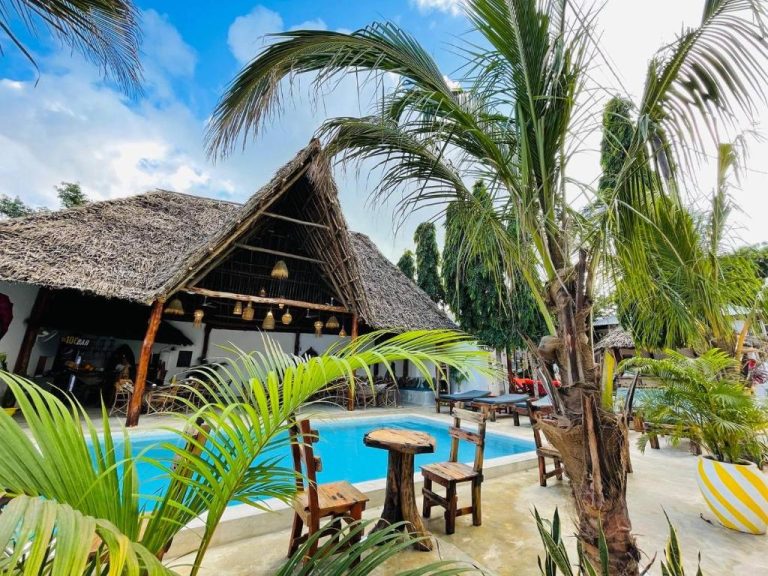 Piscina exterior rodeada de palmeras y bungalows con techo de paja en Babalao Bungalows