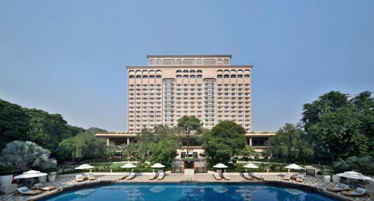 Piscina exterior con tumbonas y sombrillas del Taj Mahal Hotel en Nueva Delhi con vistas al edificio principal