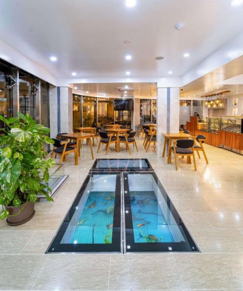 Restaurante del Marukab Plaza con suelo de cristal sobre acuario y mesas de madera con sillas