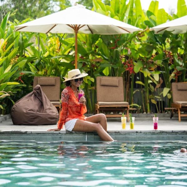 Mujer disfrutando de cócteles junto a la piscina rodeada de vegetación tropical en Bruga Boutique Hotel