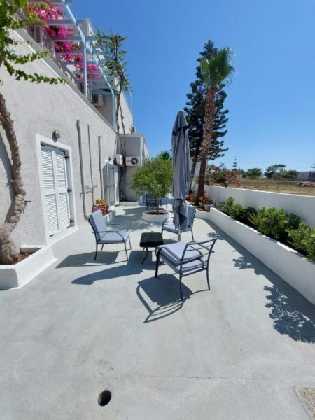 Terraza exterior con sillas y sombrilla del Alkyon Hotel, rodeada de vegetación mediterránea y cielo azul