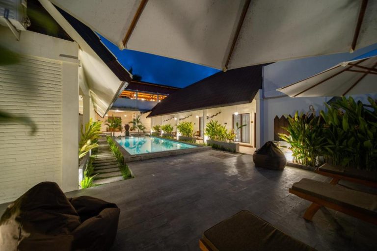 Piscina exterior iluminada de noche con jardines tropicales en Bruga Boutique Hotel Bali