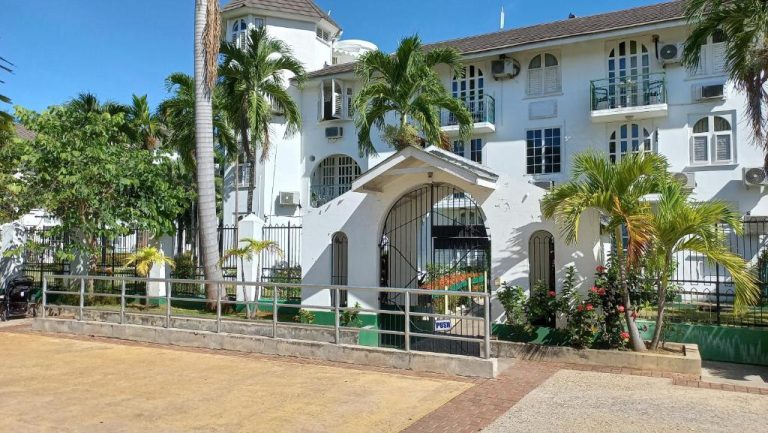 Fachada exterior blanca con palmeras tropicales y entrada principal del Beach Studio 20 en Jamaica