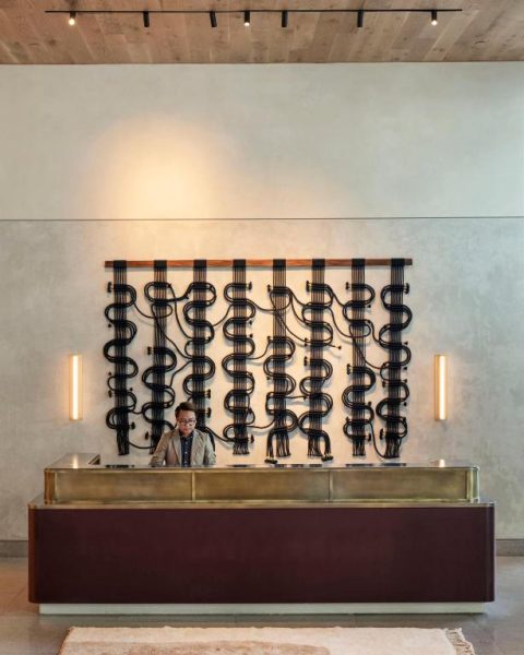 Recepción principal del ROOST Tampa con mostrador de bronce y arte mural decorativo en macramé negro