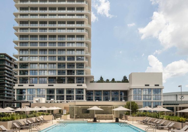 Piscina exterior con tumbonas y sombrillas del ROOST Tampa con torre de apartamentos al fondo