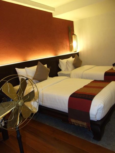 Habitación twin con decoración tradicional tailandesa y ventilador vintage en De Lanna Hotel
