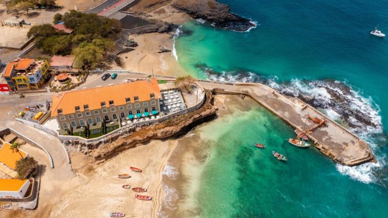 Vista aérea del Oasis Tarrafal Alfandega Suites junto al mar turquesa y playa con barcas en Cabo Verde