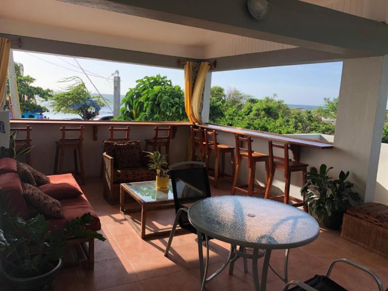 Terraza con sofás, mesas y taburetes con vistas al mar y vegetación en Airport Beach Hotel