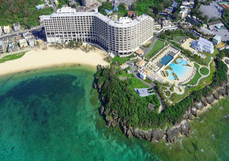 Vista aérea del Hotel Monterey Okinawa Spa & Resort con piscina exterior y playa de arena blanca