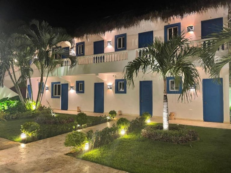 Fachada exterior iluminada de noche del Nuovo Hotel Playa Catalina con puertas azules y jardín tropical