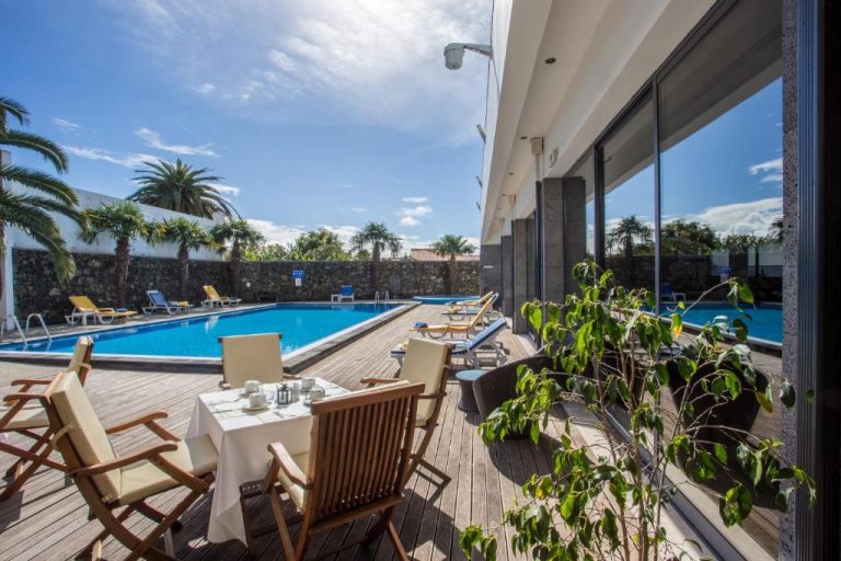 Piscina exterior con terraza de madera y tumbonas del Antillia Hotel rodeada de palmeras