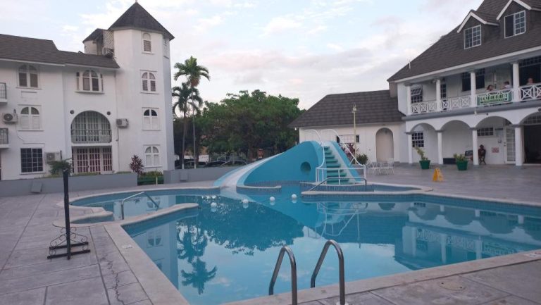 Piscina exterior con tobogán azul y escaleras del Beach Studio 20 rodeada de edificios blancos