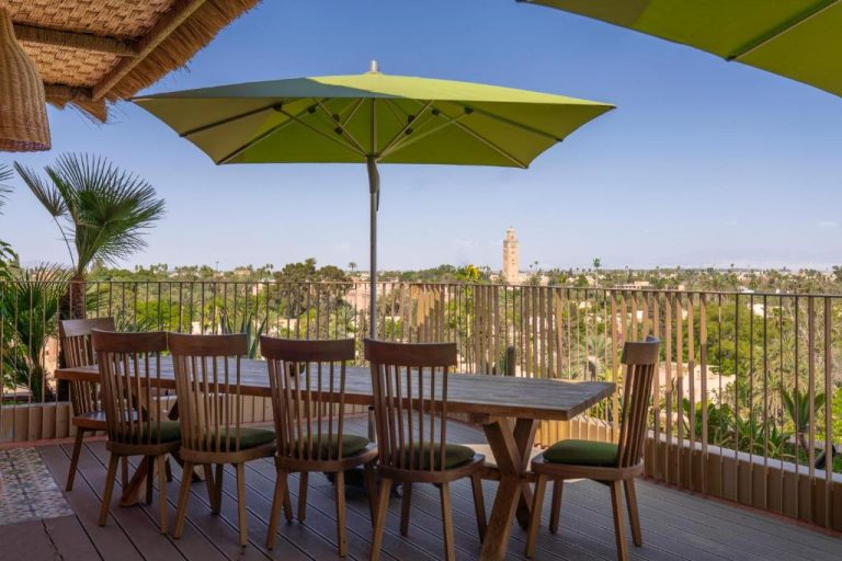 Terraza con mesa de madera y sombrilla verde del Hotel Jadali Spa con vistas a la Koutoubia de Marrakech