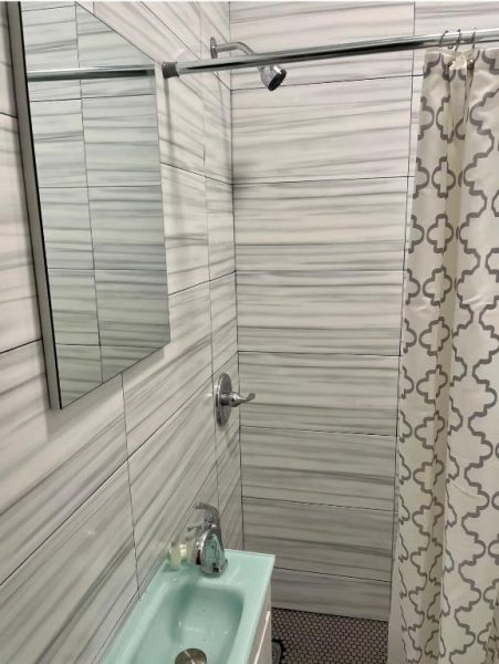 Baño moderno con ducha y azulejos grises en Navona Studios, lavabo turquesa y cortina decorativa