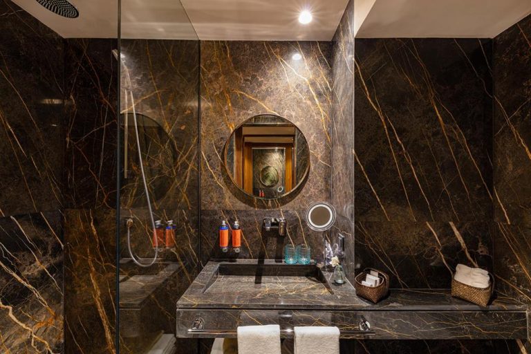 Baño de lujo con mármol negro y dorado, ducha y lavabo integrado en Hotel Jadali & Spa