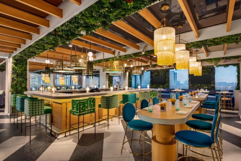 Restaurante y bar interior con vegetación tropical y sillas azules en Lake Nona Wave Hotel