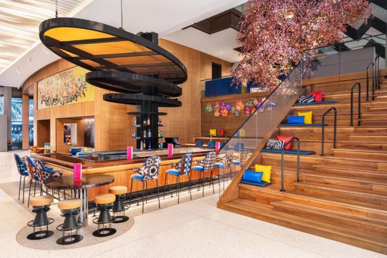 Lobby bar del Lake Nona Wave Hotel con escalera de madera, flores decorativas y coloridos cojines