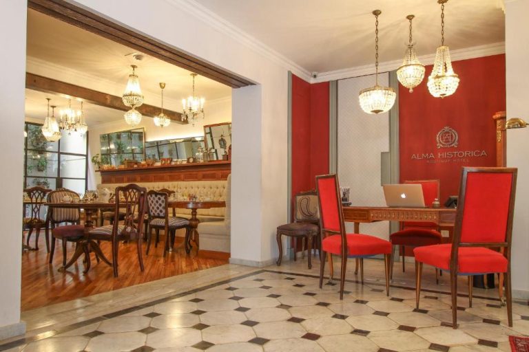 Recepción y salón comedor clásico del Alma Histórica Boutique Hotel con lámparas de araña y sillas rojas